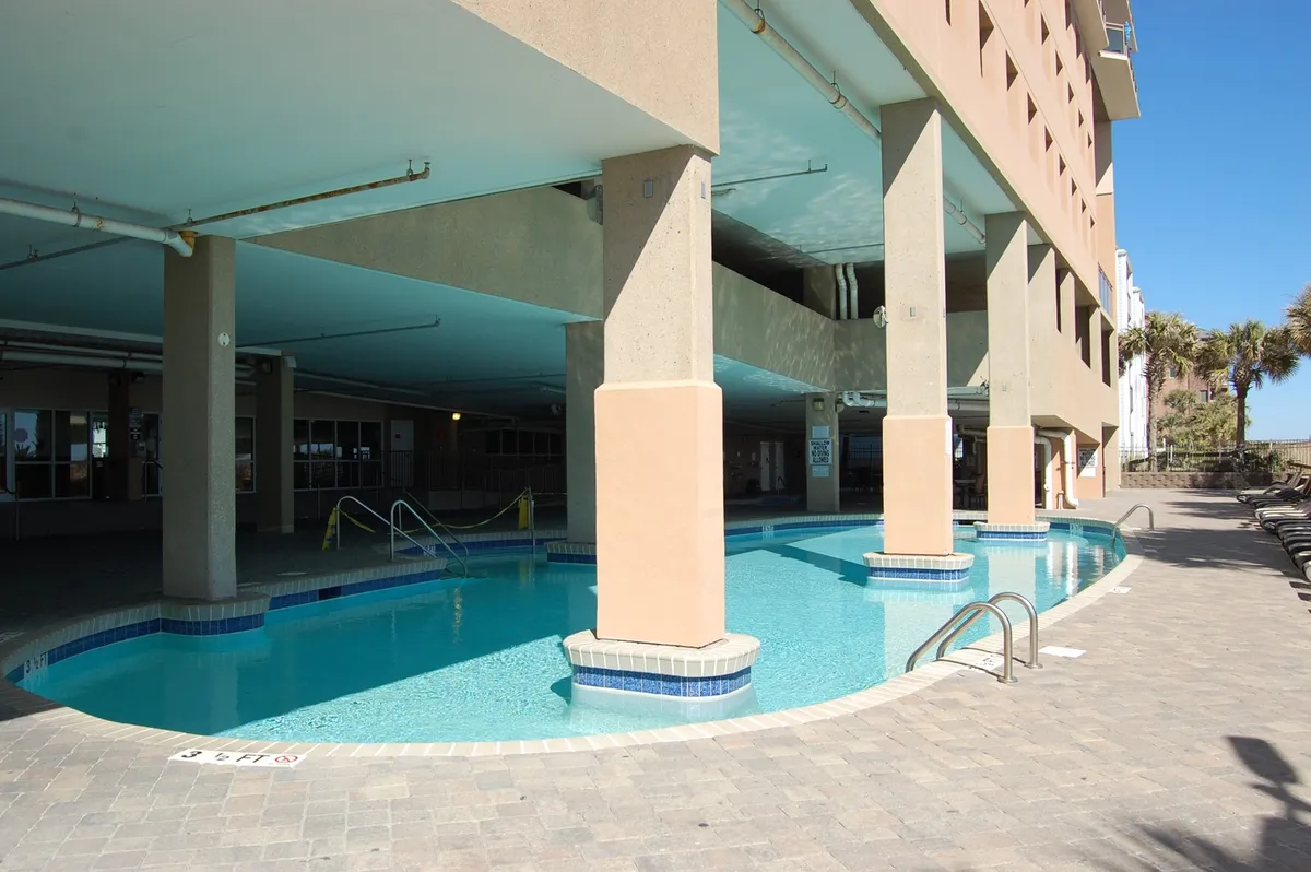 The image highlights the resort's inviting swimming pool surrounded by lounge chairs and clear blue water. Support columns add architectural interest, and the atmosphere is leisurely and relaxing—ideal for guests seeking a refreshing break from their excursions.