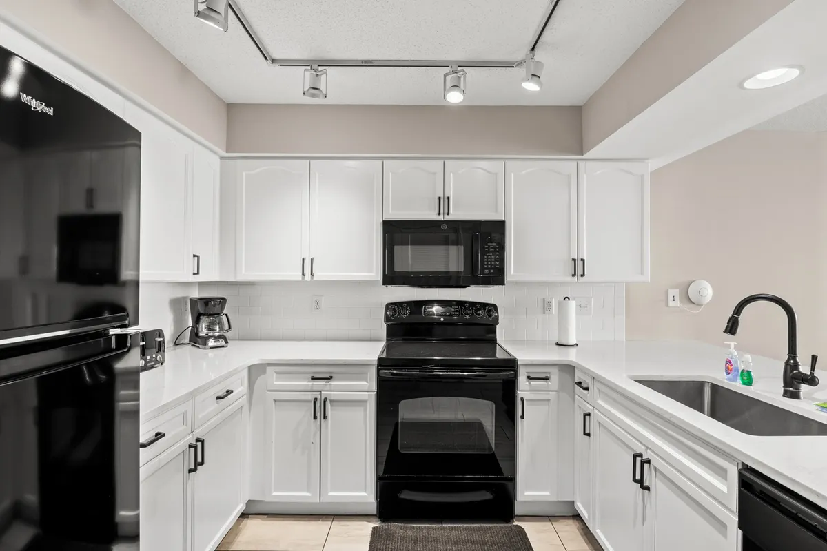 Featuring sleek black appliances, white cabinetry, granite countertops, and a convenient sink, this kitchen presents a slightly different angle. The setup is ideal for baking, cooking, and hosting, and the open sightlines reinforce the connection to living and dining areas, fostering a sense of togetherness.