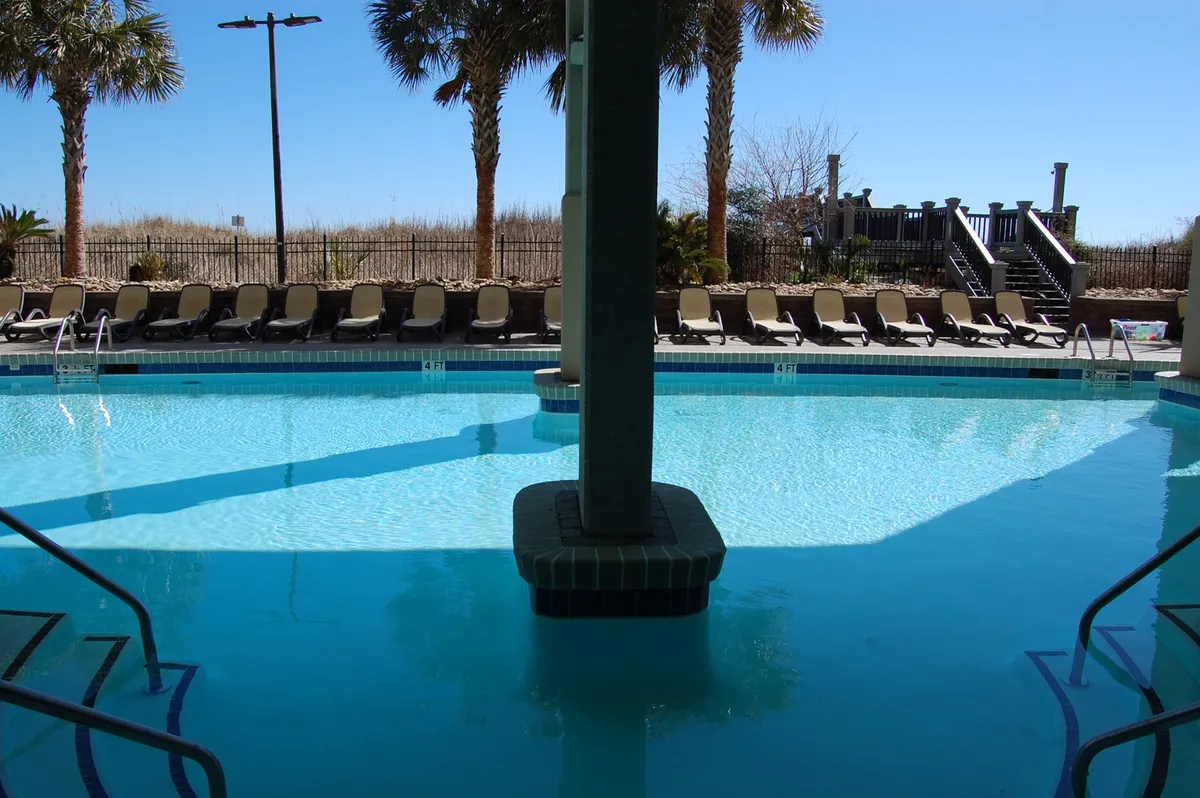 The inviting pool area at Bahama Sands features a sparkling swimming pool surrounded by lounge chairs and framed by swaying palm trees. The deck is bustling with opportunities for relaxation and group fun, ideal for families unwinding together after a day at the beach.