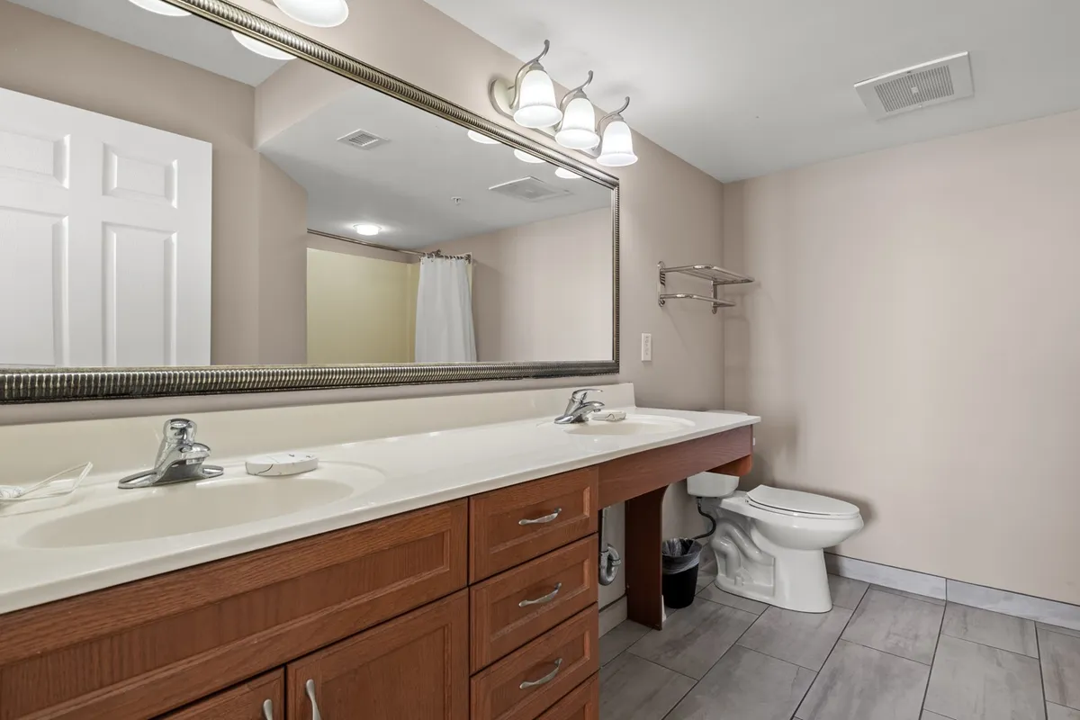 A bright, modern bathroom featuring a double sink vanity with a large mirror, sleek fixtures, and a view of a glass-enclosed shower area. The space feels fresh and accommodating, ideal for both quick morning routines and relaxing evening rituals.