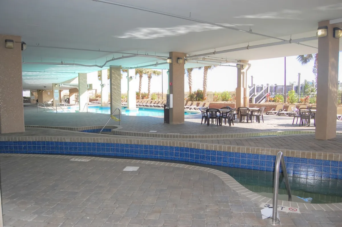 A beautifully maintained outdoor area featuring a large swimming pool, inviting jacuzzi, and several palm trees and lounge chairs. The mood is inviting yet intimate, perfect for couples to unwind together in a resort-style atmosphere.