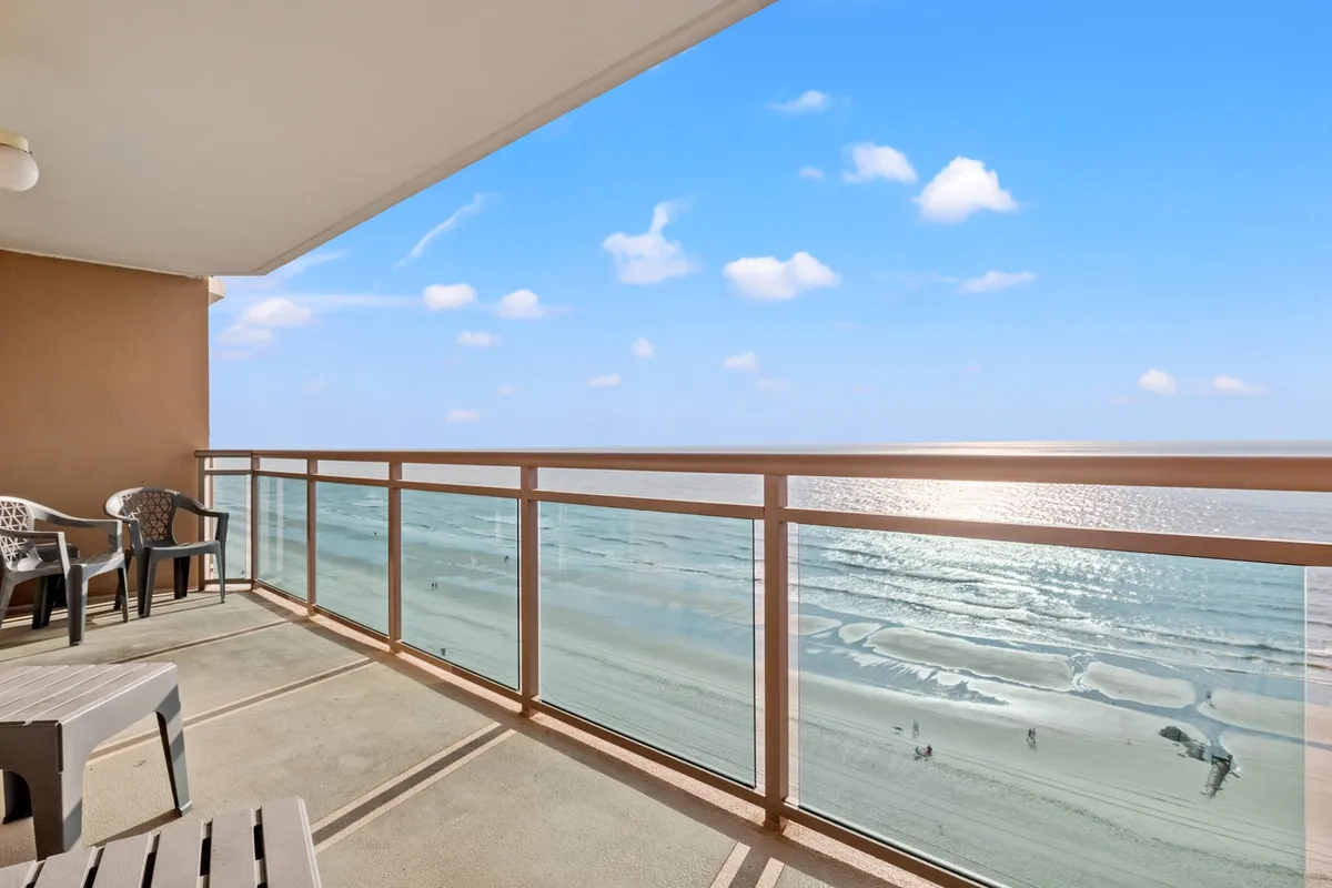 This image features a private balcony with outdoor seating, a sturdy railing, and sweeping ocean views. Soft light bathes the scene, evoking tranquil mornings and breathtaking sunsets with the sound of waves below.